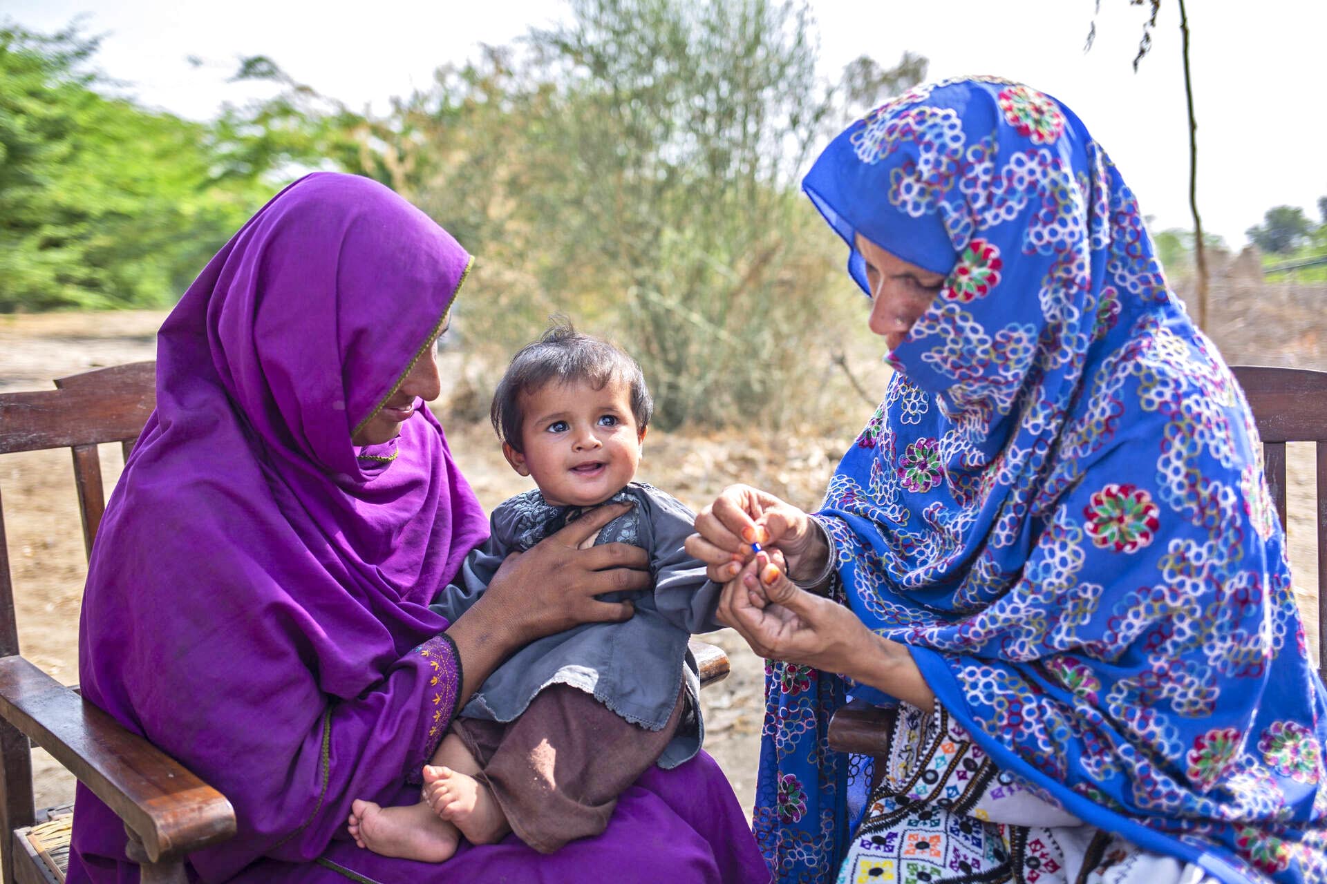 A baby sitting on his mother's lap whilst a female health worker conducts a test