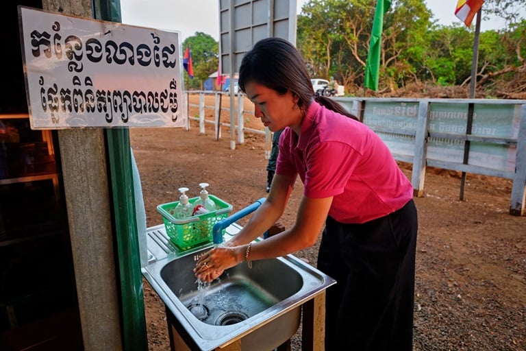 A woman bends over an outdoor sink to wash her hands.
